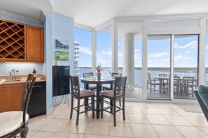 A modern kitchen with a wine rack, a dining area with a round table and chairs, and a balcony with a view of the sea. - 3 BR 3 BA spacious condo~Gulf Shores~25% DISC FOR WEEKLY RENTAL-Gulf/lagoon view (Gulf Shores)