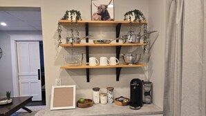 A kitchen with wooden shelves holding kitchenware, a coffee maker, and a framed picture. - ​Mainstreet Hideaway | Cozy Downtown Gem in the Heart of Powassan (Powassan)