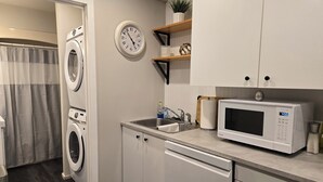 A compact kitchen with a built-in microwave, a sink, and a washing machine. - ​Mainstreet Hideaway | Cozy Downtown Gem in the Heart of Powassan (Powassan)