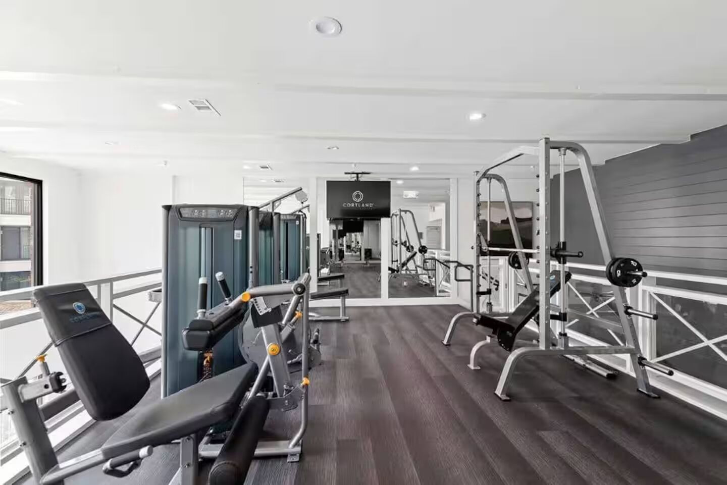 A modern gym with various exercise equipment, including treadmills, weight machines, and a mirrored wall.
