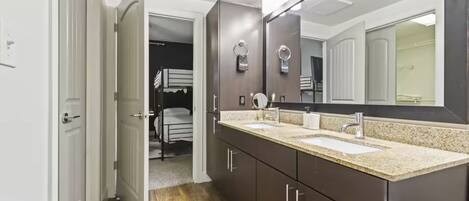 Un baño moderno con lavamanos doble, muebles oscuros y un espejo grande.