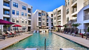 A swimming pool with lounge chairs and umbrellas, surrounded by multi-story buildings with balconies. - Great for Children with bunk Beds (Frisco)