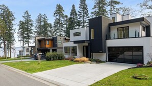 Ein modernes, zweistöckiges Haus mit Garage, umgeben von einem gepflegten Rasen und hohen Bäumen.