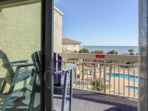 Ein Balkon mit Blick auf ein Schwimmbad und einen Strand, ein Verbotsschild für Grillen sowie ein Gebäude mit einer strukturierten Wand.