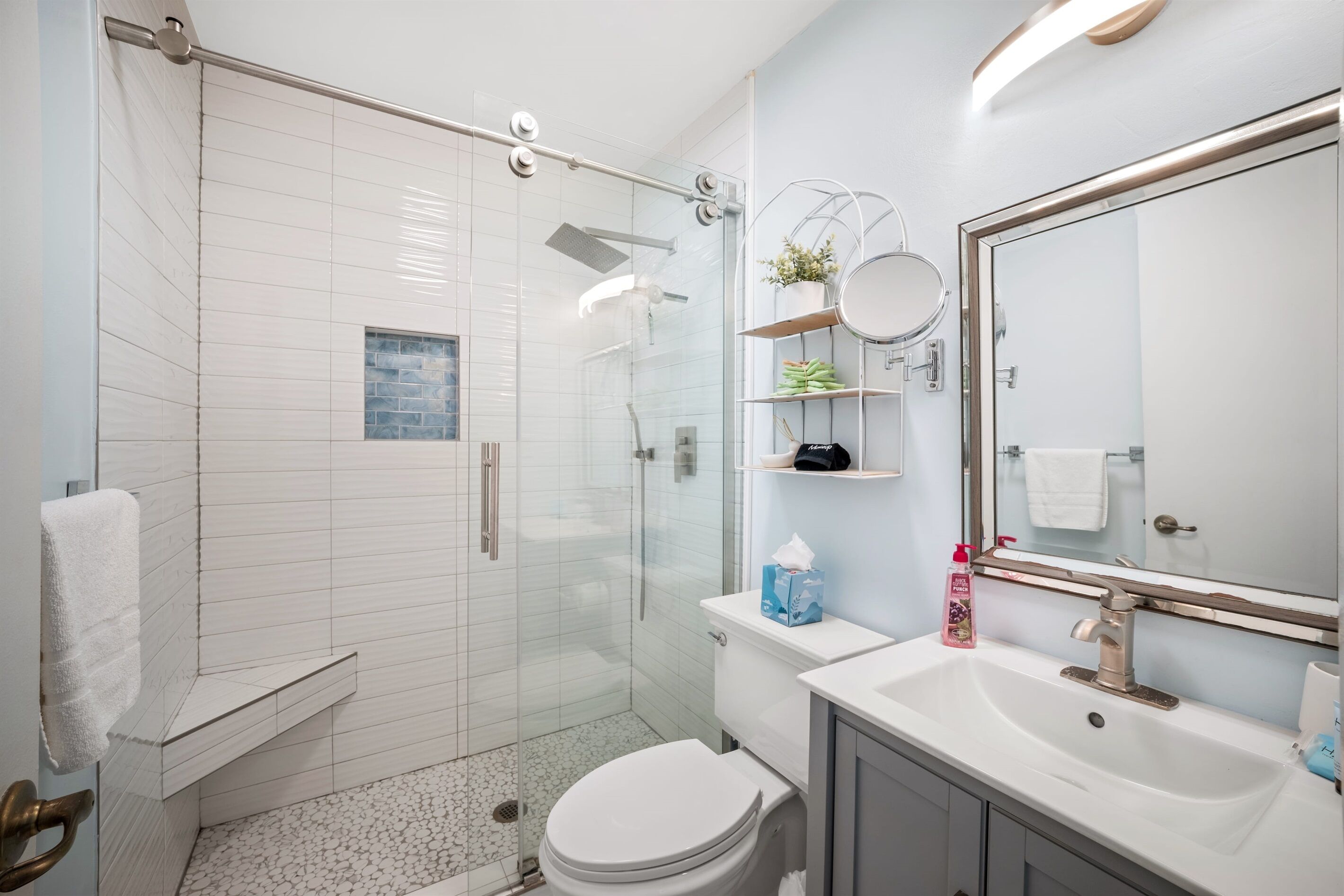 Une salle de bain moderne avec une douche à parois de verre, des toilettes blanches, un lavabo avec un miroir et un porte-serviettes.