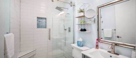 Une salle de bain moderne avec une douche à parois de verre, des toilettes blanches, un lavabo avec un miroir et un porte-serviettes.