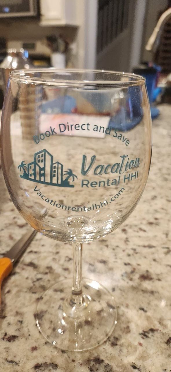 A clear glass wine glass with embossed text and a logo, placed on a granite countertop.