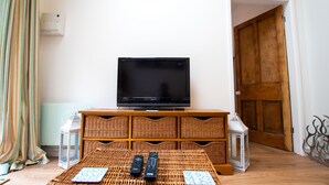 Ein Wohnzimmer mit Fernseher auf einem Holzboden, Korbmöbeln und zwei Fernbedienungen auf einer gewebten Matte.