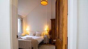 Ein Schlafzimmer mit Bett, Nachttischen, einem Holzschrank, einer Hängeleuchte und einem Fenster mit Vorhängen.