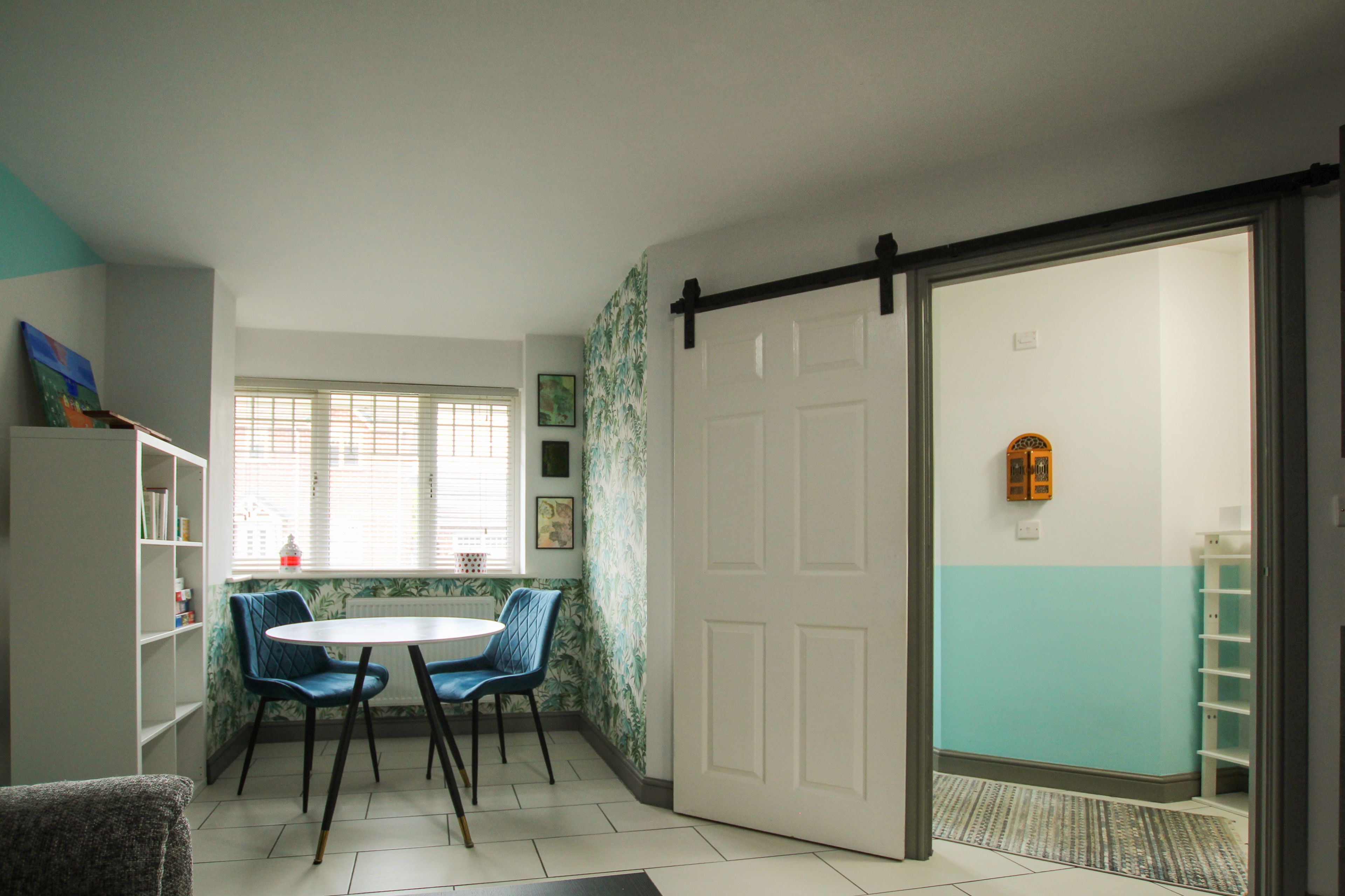 Una habitació amb una porta blanca, una cadira blava, un taulell blanc i una prestatgeria.