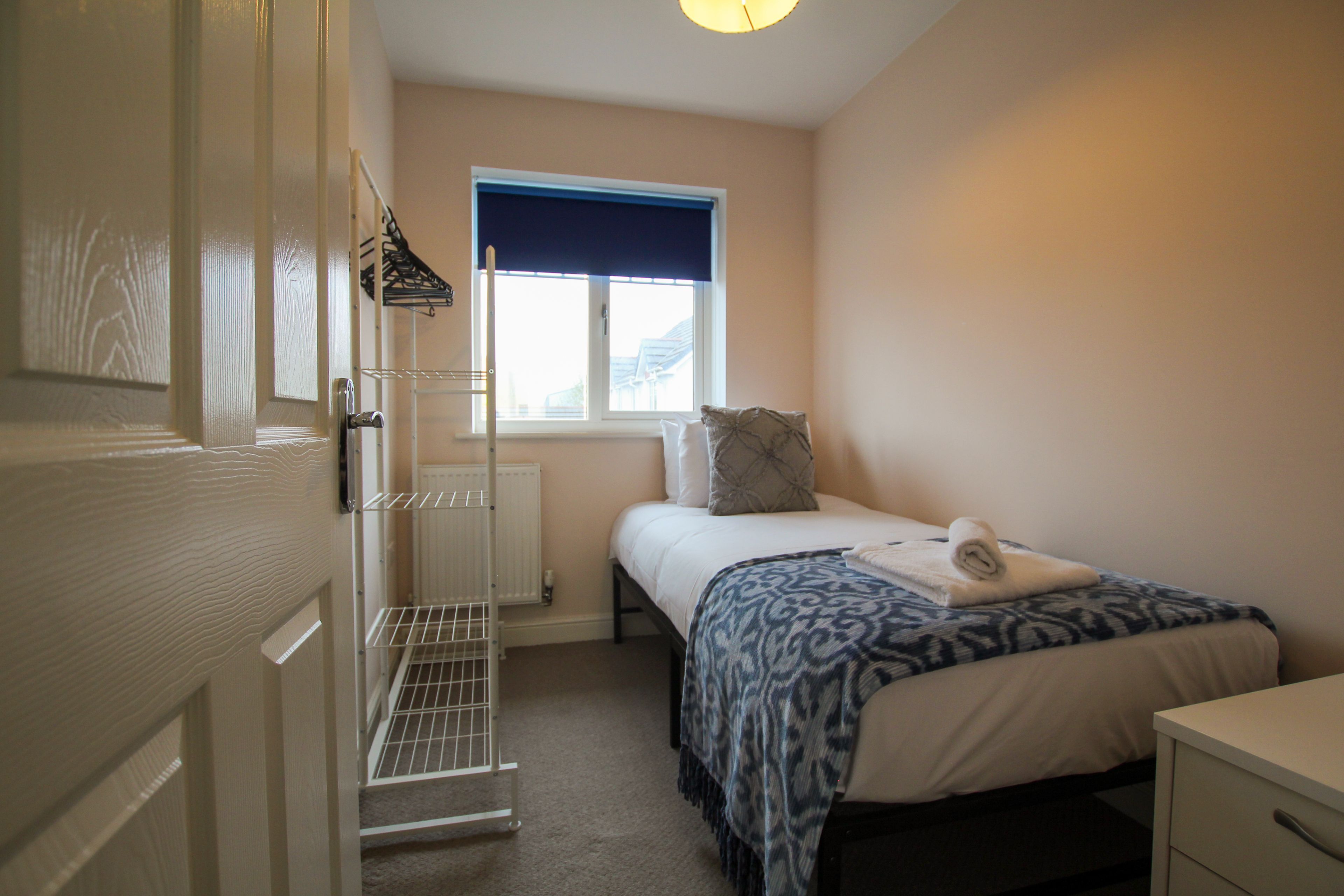 A bedroom with a bed, a window with a blue blind, a radiator, a white wardrobe, and a white door.