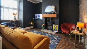 Ein Wohnzimmer mit Sofa, einem roten Sessel, einem Fernseher, einem Kamin und einer Lampe.