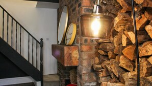 Eine Treppe mit Metallgeländer, eine Holzwand mit gestapeltem Holz und ein Kupfertopf an der Wand.