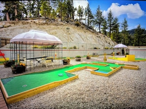 Ein Minigolfplatz mit mehreren Bahnen, einer Sitzgelegenheit und Bäumen sowie einem felsigen Hügel im Hintergrund.