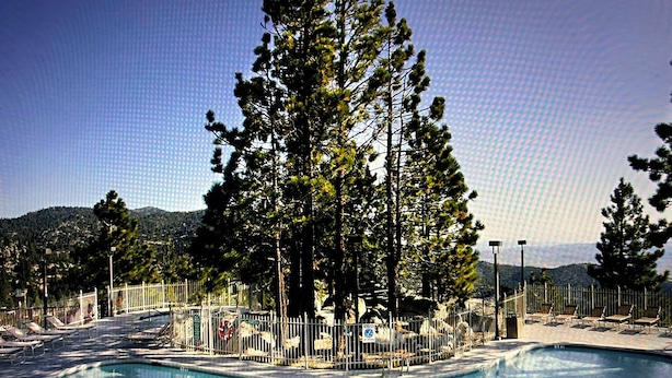 Una piscina circondata da una recinzione, con alberi alti e montagne sullo sfondo.
