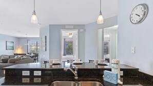 A modern kitchen with a central island, double sinks, pendant lighting, and a clock on the wall. - 4840-303 Family Condo with Large Balcony & Resort (Orlando)