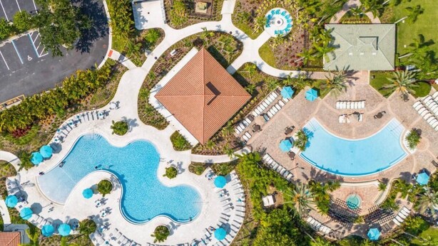 En vy från ovan av ett semesterområde med en central pool, solstolar och ett separat poolområde.