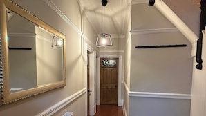 En hall med en stor spegel, en hängande lampa, ett element och en trädörr längst ner.