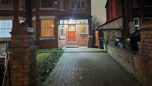 Ett traditionellt hus byggt av tegel med en central entré, en synlig skorsten och en stenlagd uppfart som leder fram till ytterdörren.