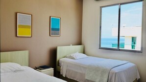 Une chambre d’hôtel avec deux lits, une fenêtre donnant sur la mer et deux œuvres d’art encadrées accrochées au mur.