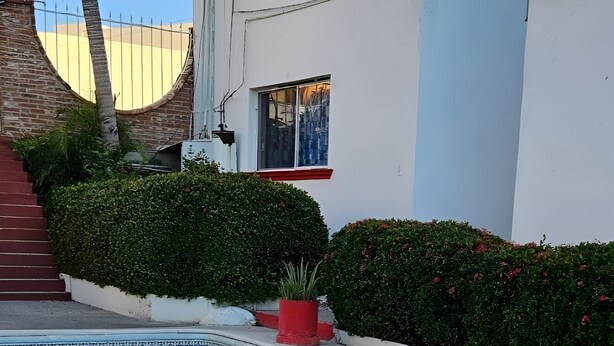 A swimming pool with a clear blue water surface, surrounded by a paved area and a white building with a red trim. - Hotel Villas Punta Peñasco (Acapulco)