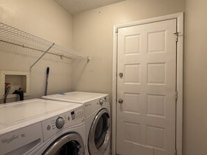 A laundry room with two front-loading washers, a metal shelf, and a white door. - Best of Destin & Fort Walton Coastal Retreat (Fort Walton Beach)