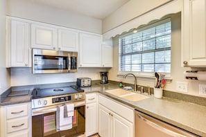 A kitchen with white cabinets, a stainless steel microwave, a toaster, a coffee maker, and a window with blinds. - Best of Destin & Fort Walton Coastal Retreat (Fort Walton Beach)