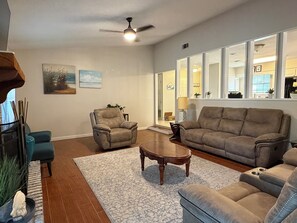 A spacious living room with a large window, a ceiling fan, and a view into the kitchen. - Best of Destin & Fort Walton Coastal Retreat (Fort Walton Beach)