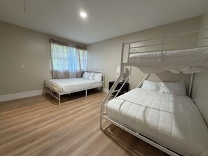 Une chambre avec deux lits superposés, un lit simple, une table de chevet et une fenêtre avec des rideaux.