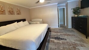 Una camera da letto con un letto, una culla, un ventilatore a soffitto, una TV e un corridoio che conduce a un'altra stanza.