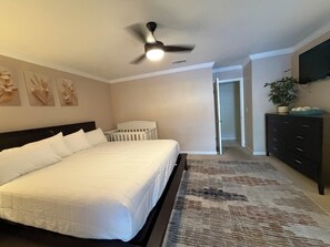 A bedroom with a bed, a crib, a ceiling fan, a TV, and a hallway leading to another room. - Best of Destin & Fort Walton Coastal Retreat (Fort Walton Beach)