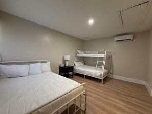 Ein Schlafzimmer mit Etagenbett, einem Einzelbett, einem Nachttisch mit Lampe und einer Wandklimaanlage.