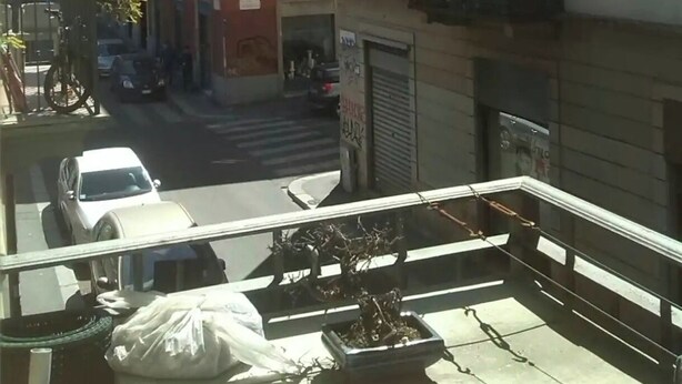 A balcony with a view of a street, a parked car, and a building with a closed shutter. - Wooden loft with balcony (metro and services under the house) sleeps 4 (Milano)