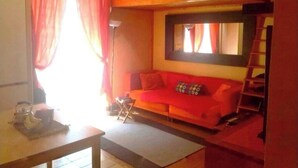 A cozy room with a red sofa, a small table with a kettle, and a window with curtains. - Wooden loft with balcony (metro and services under the house) sleeps 4 (Milano)