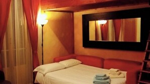 A single bed with a white mattress and pillows, a bedside table, a mirror on the wall, and a red headboard. - Wooden loft with balcony (metro and services under the house) sleeps 4 (Milano)
