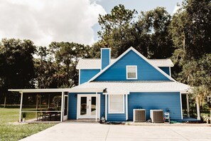 A two-story blue house with a covered porch, a chimney, and two air conditioning units. - Spacious 4-bedroom country house in peaceful Fruitland Park with AC (Fruitland Park)