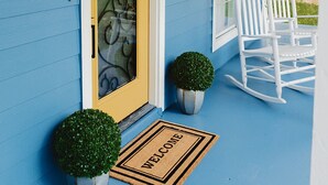 A blue house with a yellow door, white rocking chairs, and a welcome mat.