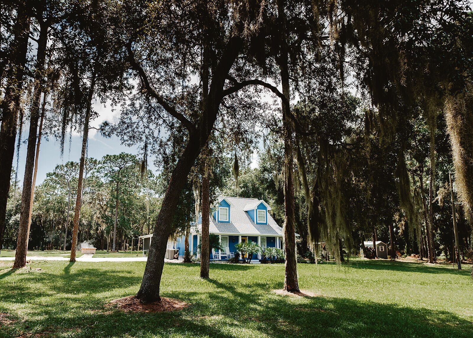 A house with a blue roof and white trim, surrounded by tall trees and a well-maintained lawn.