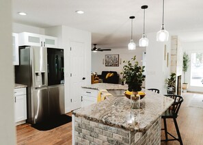 A modern kitchen with a granite island, stainless steel appliances, pendant lighting, and a dining area with a black chair. - Spacious 4-bedroom country house in peaceful Fruitland Park with AC (Fruitland Park)