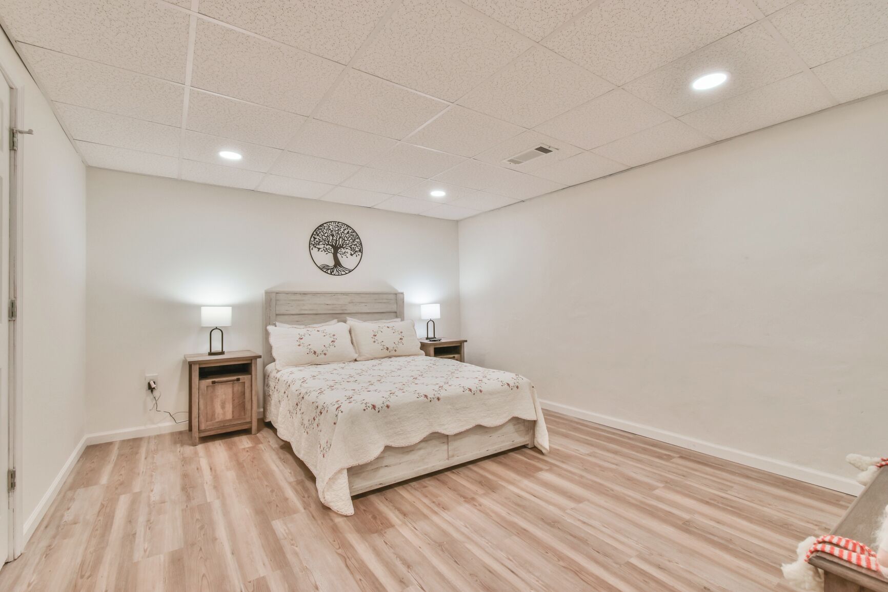 A bedroom with a bed, nightstands, a wall-mounted tree decoration, and a wooden floor.