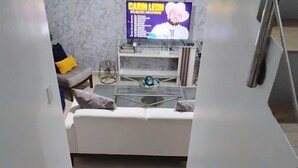 Una sala de estar moderna con un sofá blanco, una mesa de centro de vidrio y un televisor de pantalla plana mostrando 'CARIN LEON'.