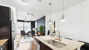 A modern kitchen with a granite countertop, stainless steel sink, and a ceiling fan. - Lux 1B w Pool Near Toyota HQ (Frisco)