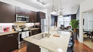 A modern kitchen with stainless steel appliances, granite countertops, and dark cabinetry. - Lux 1B w Pool Near Toyota HQ (Frisco)