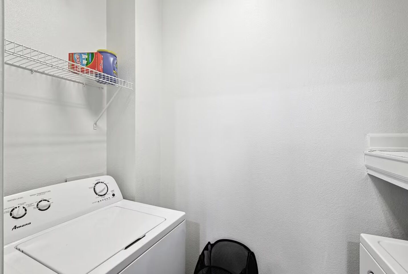 A laundry area with a white washing machine, a shelf with detergent, and a dryer.