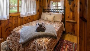 Un dormitorio con paneles de madera, una cama, dos ventanas con cortinas, una lámpara de techo y un ventilador.