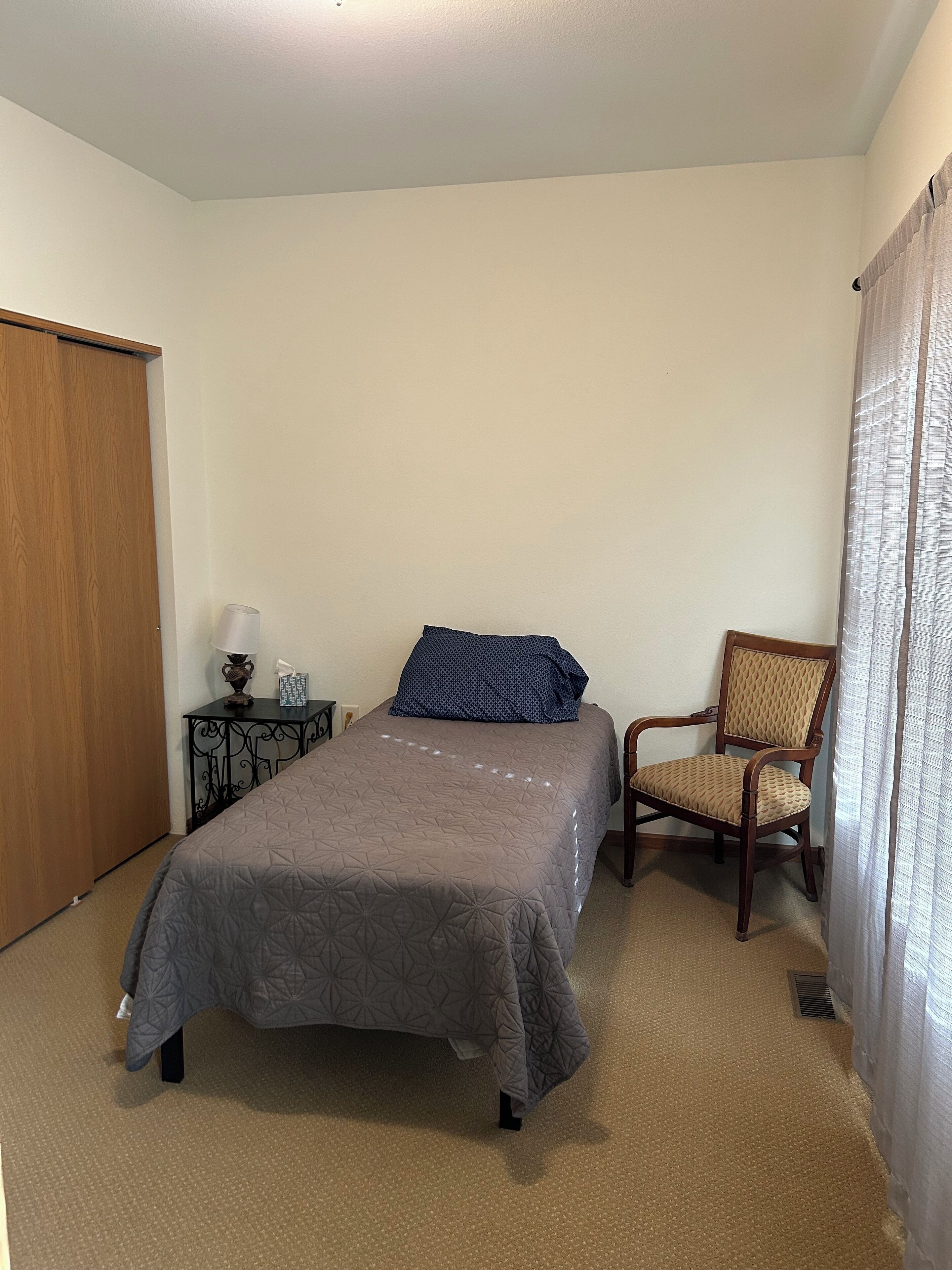 Een slaapkamer met een bed, een stoel, een nachtkastje en een kledingkast.