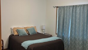 Une chambre à coucher avec un lit, une table de chevet, une lampe et une fenêtre avec des rideaux.