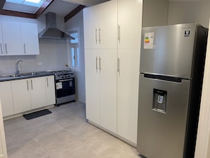 A modern kitchen with white cabinets, a stainless steel refrigerator, a gas stove, and a water dispenser. - Spacious and comfortable house, excellent heating. (Punta Arenas)