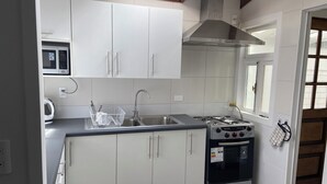 A compact kitchen with white cabinets, a stainless steel sink, a microwave, and a gas stove. - Spacious and comfortable house, excellent heating. (Punta Arenas)