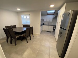 A compact kitchen with a dining area, a refrigerator, and a window with blinds. - Spacious and comfortable house, excellent heating. (Punta Arenas)